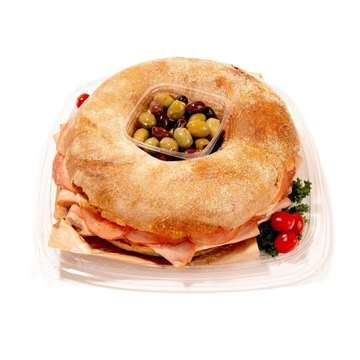 Ring-shaped muffaletta sandwich tray with deli meats, cheese, central olive mix, and cherry tomatoes garnish.